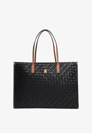 Sort vævet shoppingtaske med brune læderhåndtag og en lille gylden logo centreret under håndtagsfastgørelsen.