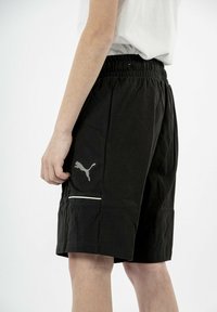 Shorts atléticos negros con cintura elástica, con un logo gris en el muslo y una franja de acento blanca cerca del bolsillo.