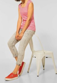 Červený a bílý pruhovaný bezrukávový top, světle šedé vybledlé džíny, oranžové tenisky a bílá kovová židle. Zaměření na detaily každodenního oblečení.