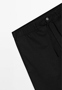 Pantaloni neri con vita elasticizzata e cordoncino, con chiusura a bottone, esposti su uno sfondo bianco.