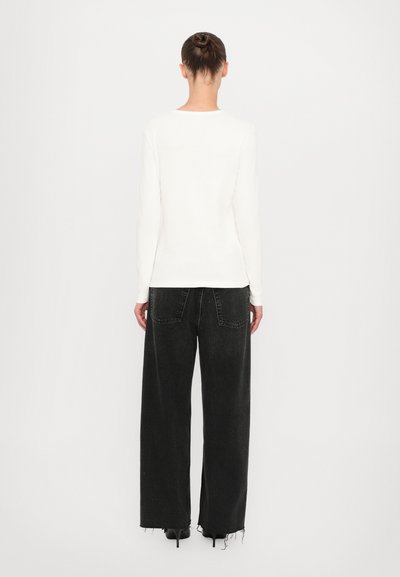 White long-sleeve top with ribbed texture, paired with loose black jeans featuring frayed hems and two back pockets.