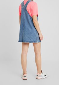 Kesel denim berwarna biru muda, dengan bodice yang pas, rok melebar, dan tali yang dapat disesuaikan. Dipakai di atas kaos berwarna pink dengan sepatu sneakers putih.