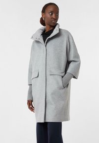 Hellgrauer Wollmantel mit hohem Kragen, Taschen vorne und gerippten Strickbündchen. Lässige Passform mit weicher Textur und minimalistischem Design.