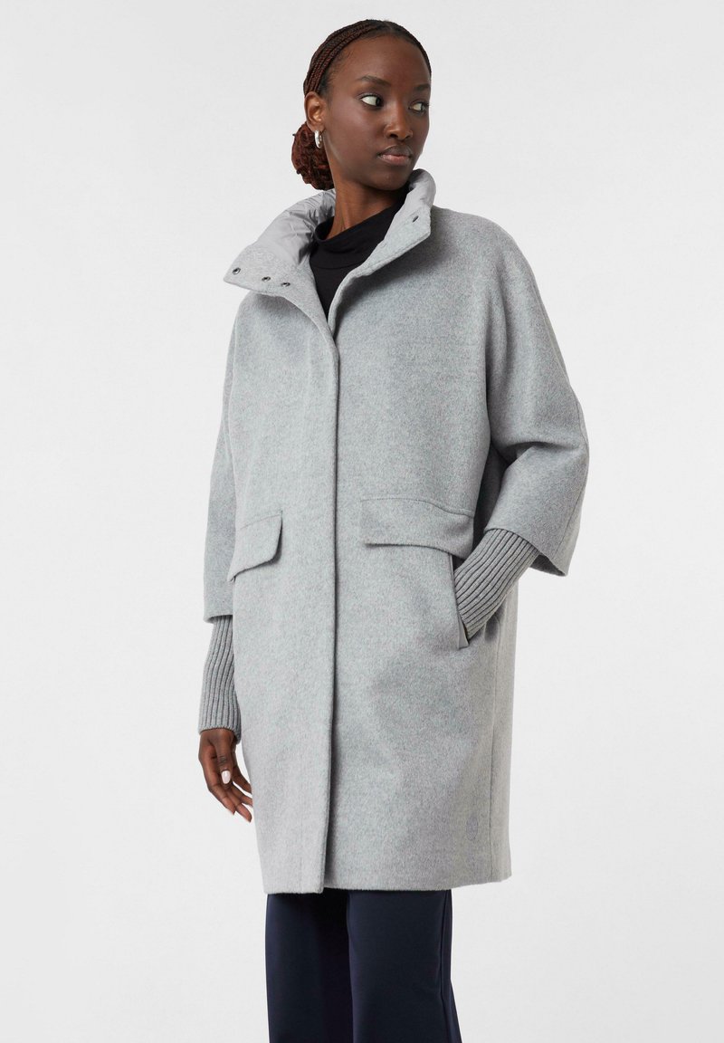 Hellgrauer Wollmantel mit hohem Kragen, Taschen vorne und gerippten Strickbündchen. Lässige Passform mit weicher Textur und minimalistischem Design.