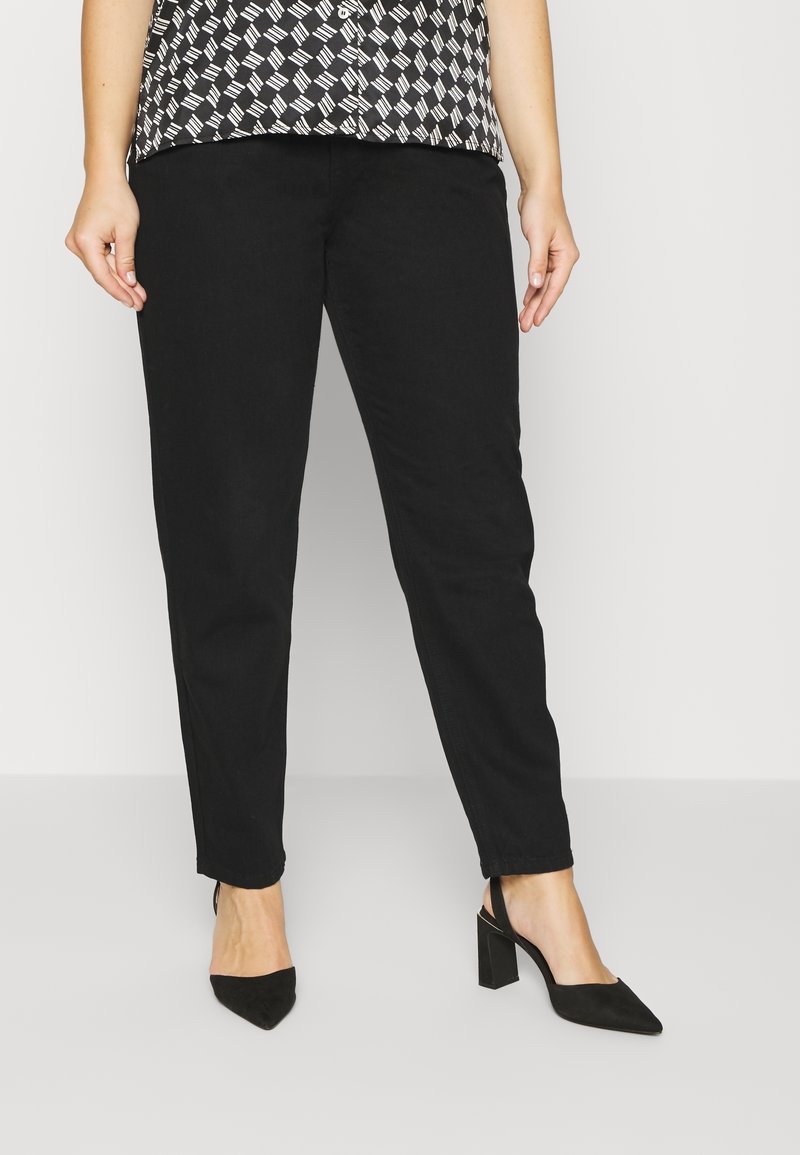 Jean noir fuselé en denim, associé à des talons aiguilles noirs à bout pointu. Le haut est une blouse à motif noir et blanc.