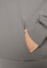Grauer Sweatshirtstoff mit einer Seitentasche; sichtbare Nahtdetails und gerippte Bündchen. Schlichte Textur, lässiges Design ohne Muster.