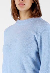 Maglione azzurro chiaro realizzato in un tessuto morbido e texture. Presenta un collo a girocollo a coste e maniche lunghe con una vestibilità rilassata.