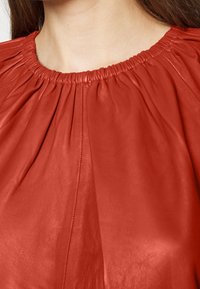 Haut en cuir rouge avec un col froncé, doté d'une texture douce et lisse ainsi que de détails plissés s'étendant à partir du col.