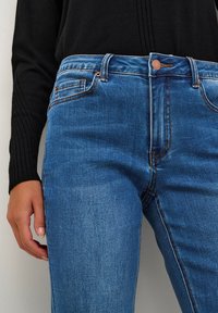 Blå denimjeans med medelhög midja, fem fickor och koppardetaljer. Tyget har en något blekt struktur och rak passform.