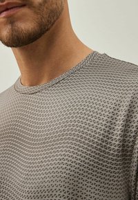 Grå kortærmet skjorte med struktureret geometrisk mønster af trekanter, med en rund hals og glat stof. Ingen synlige logoer eller udsmykninger.
