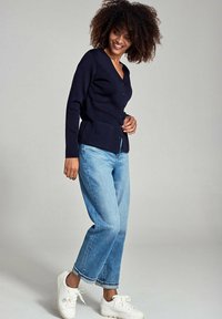 Marineblauwe cardigan met een V-hals en knoopsluiting, gecombineerd met lichtblauwe wijde jeans en witte sneakers. Glad textuur, casual pasvorm.