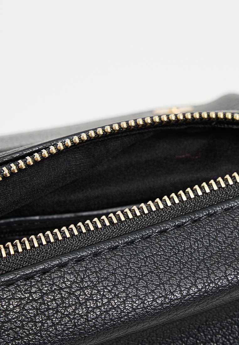Sac en cuir texturé noir avec une fermeture éclair dorée, dévoilant une doublure intérieure noire. Présente un design rectangulaire simple.