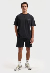 Zwarte katoenen T-shirt met korte mouwen en een ronde halslijn, gecombineerd met zwarte shorts. Opvallend logo detail op het T-shirt en de shorts.