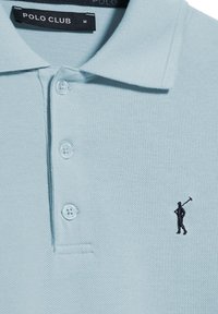 Polo de color azul claro hecho de tejido texturizado, con tres botones en la parte frontal y un logotipo bordado en negro de una figura sosteniendo un mazo.