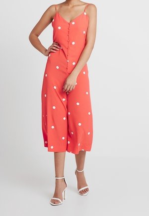 Korallinvärinen haalari, jossa valkoiset pilkut, spagettihihnat ja napit edessä. Löysä, lyhyt mitoitus ja sileä pinta.