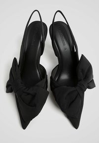Zwarte slingback hakken met een spitse neus, stoffen strikaccent op elke hak en een gladde, glanzende binnenvoering.