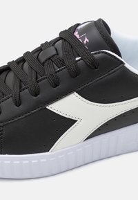 Scarpa da ginnastica nera con tomaia in pelle liscia, accenti bianchi e suola in gomma testurizzata. Presenta lacci neri e dettagli perforati.