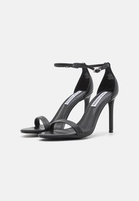 Sandales à talons hauts noires avec une fine bride de cheville, deux brides avant, une texture en cuir lisse et un design à talon aiguille.