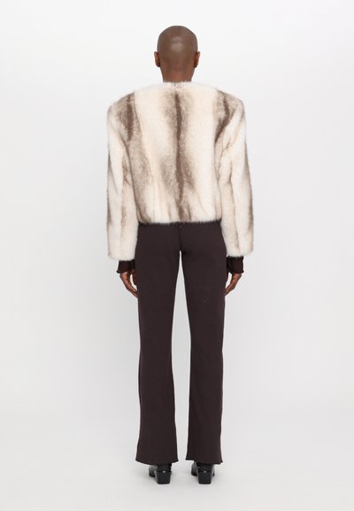 Flauschige, cremefarbene und braun gemusterte Jacke mit einem cropped Design, kombiniert mit engen, dunkelbraunen Hosen mit ausgestellten Säumen.