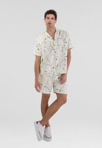 Kurzes Kurzarm-Hemd und Shorts-Set in Creme mit abstrakten schwarzen und blauen Mustern. Hat eine lockere Passform und solide schwarze Knöpfe.