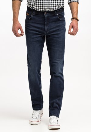 Granatowe dżinsy o slim fit, z przednimi kieszeniami i klasycznym zapięciem na guziki, w połączeniu z białymi trampkami.