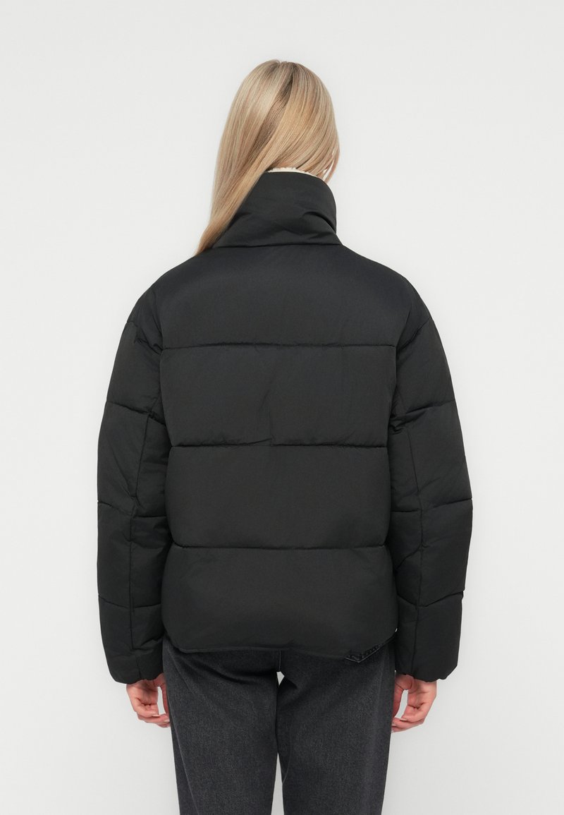 Doudoune noire avec un col haut, motif matelassé et coupe décontractée. Caractéristiques des manches longues et une finition texturée.