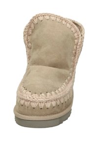 Pantofole in suede beige con suola spessa e imbottita. Presentano una decorativa cucitura intrecciata lungo il bordo. Design con punta rotonda e texture morbida.
