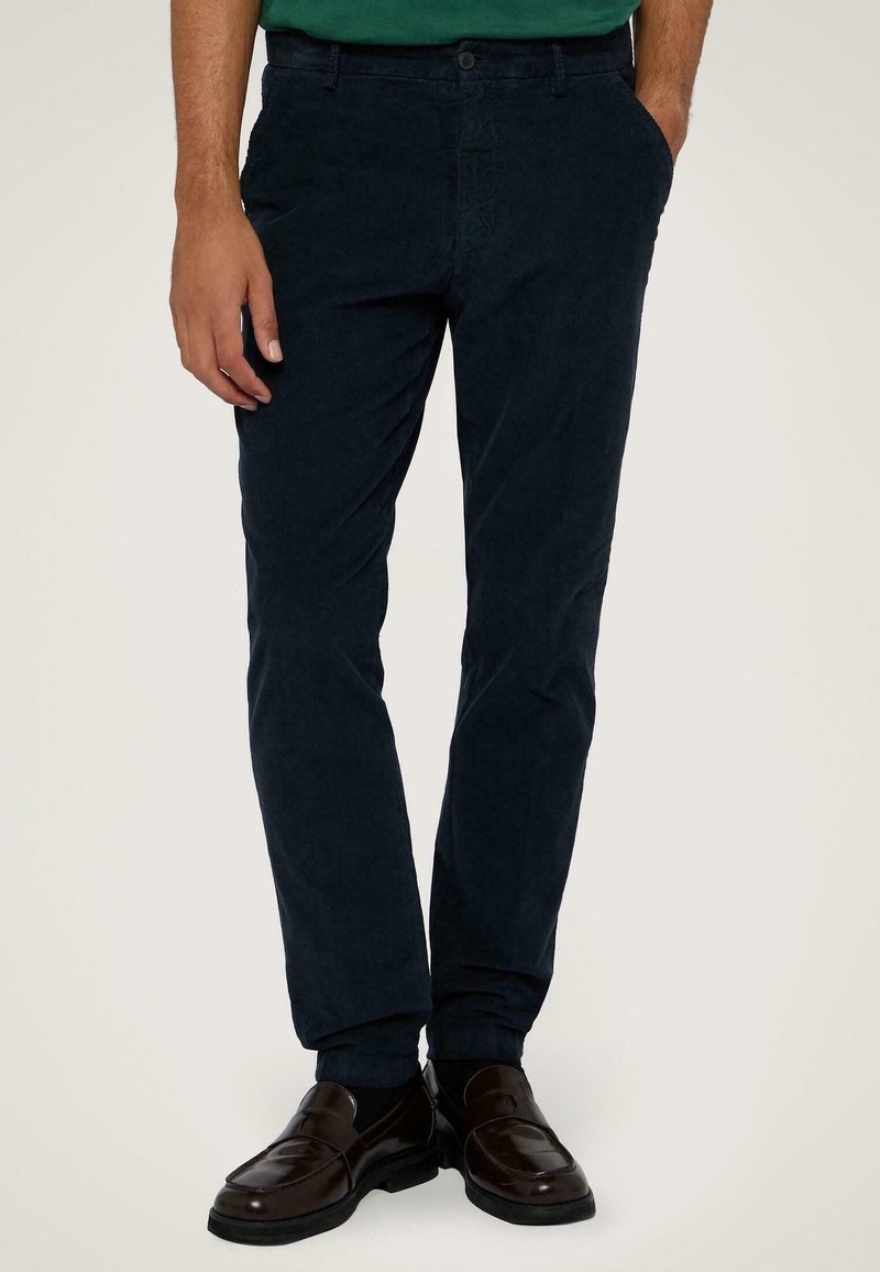 Námořnické bavlněné kalhoty s úzkým střihem, obsahující přední kapsy a hladkou texturu, spárované s tmavě hnědými mokasíny.