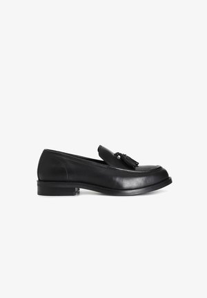 Black leather loafers featuring a rounded toe, flat heel, and a decorative tassel on the vamp. Smooth texture with minimal stitching details.
