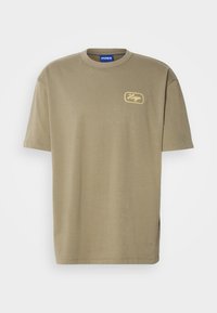 Oliven grøn T-shirt lavet af bomuld, med rund hals og korte ærmer, samt et gult broderet "Hugo" logo på venstre bryst.