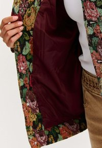 Wielokolorowa kurtka w kwiatowy wzór z bordowym podszewką; z zatrzaskami i teksturowanym materiałem.