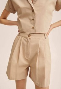 Ensemble court beige en coton léger comprenant un haut à manches courtes avec col et boutons sur le devant, ainsi qu'un short plissé avec fermeture à boutons sur le devant.