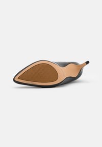 Chaussure à talons hauts noire avec un bout pointu, semelle en caoutchouc texturé et semelle intérieure beige. Présente une silhouette élancée et un design épuré.