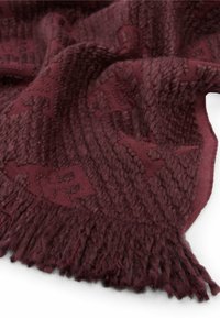 Bordowy, pleciony koc z teksturowanym wzorem, z frędzlami na brzegach i miękkim, puszystym wyglądem.