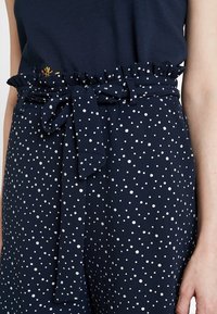 Granatowe spodnie w białe groszki, z marszczonym pasem i wiązaną kokardą z przodu. Gładka faktura.