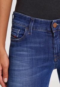 Dark blue denim jeans with a fitted design, featuring a button closure, front pockets, and subtle fading effects.