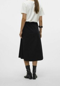 Jupe midi noire avec un design évasé, fabriquée dans un tissu texturé. Associée à un t-shirt blanc et des bottes à talons noires.