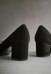 Pantofi cu toc înalt din suede negru, cu un design cu vârf ascuțit și toc masiv, având o textură netedă și o culoare solidă neagră.