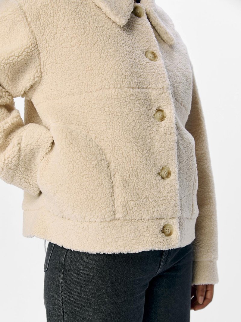 Kremowa polarowa kurtka z kołnierzykiem, zapinana na guziki z przodu oraz z bocznymi kieszeniami. Teksturowany materiał o miękkim, ciepłym wyglądzie.