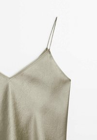 Camisole en satin beige clair avec fines bretelles spaghetti et détail subtil de tissu texturé sur fond blanc.