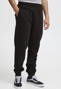 Sorte bomulds sweats med elastisk talje, sidelommer og ribbede manchetter, parret med marineblå sneakers med hvide detaljer.
