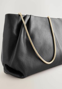 Schwarze Ledertasche mit strukturierten Oberflächen, ausgestattet mit einem goldenen Kettenriemen und einem gefalteten Design, das eine weiche, strukturierte Form zeigt.