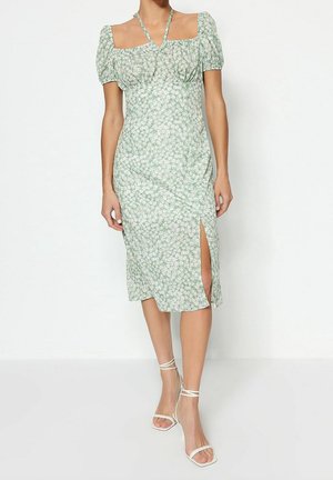 Robe midi florale verte avec des manches bouffantes courtes, des liens au niveau de la poitrine et une fente sur le côté. Fabriquée en tissu léger avec une silhouette ajustée.