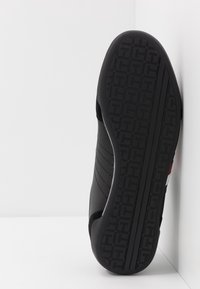 Sneaker nera con suola in gomma testurizzata, caratterizzata da cuciture orizzontali sulla parte superiore e un design a motivo sulla suola.