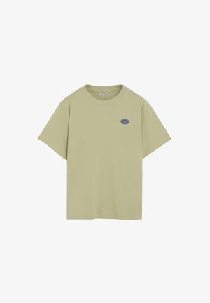 Camiseta beige de manga corta con cuello redondo y pequeño logo circular azul en el lado izquierdo del pecho que dice "Peach Freshfruit 0993".