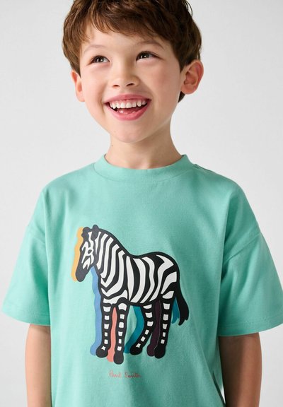 Smilende ung dreng iført en mintgrøn T-shirt med en farverig zebra grafik og teksten "Paul Smith" under.