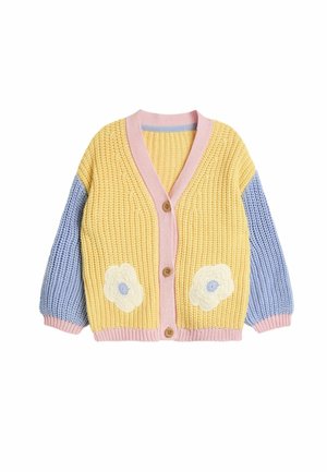 Gul strikket cardigan med blå ærmer og lyserød kant. Har to hvide blomsterbroderier og lukkes med træknapper.
