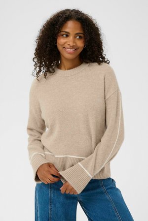 Beige strikket sweater med rund halsudskæring, ribbede manchetter og en kontrastfarvet hvid stribe i kanten, parret med blå denim jeans.