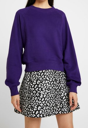 Sweatshirt violet avec un col rond et des manches raglan, associé à une jupe noire avec un motif léopard blanc.