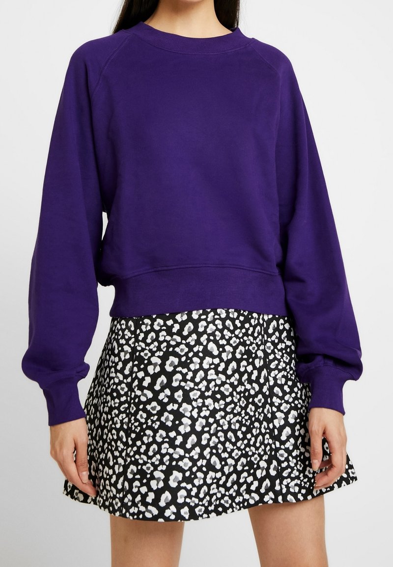 Lila Sweatshirt mit Rundhalsausschnitt und Raglanärmeln, kombiniert mit einem schwarzen Rock, der ein weißes Leopardenmuster aufweist.